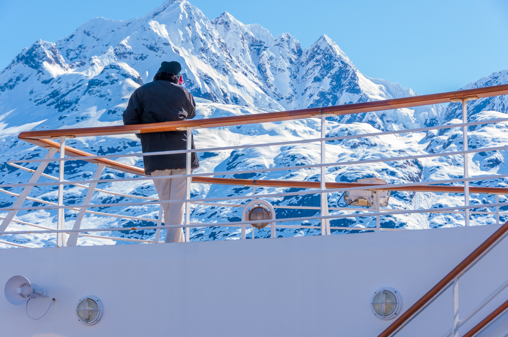 Man admiring snow covered mountain on deck of cruise ship.
