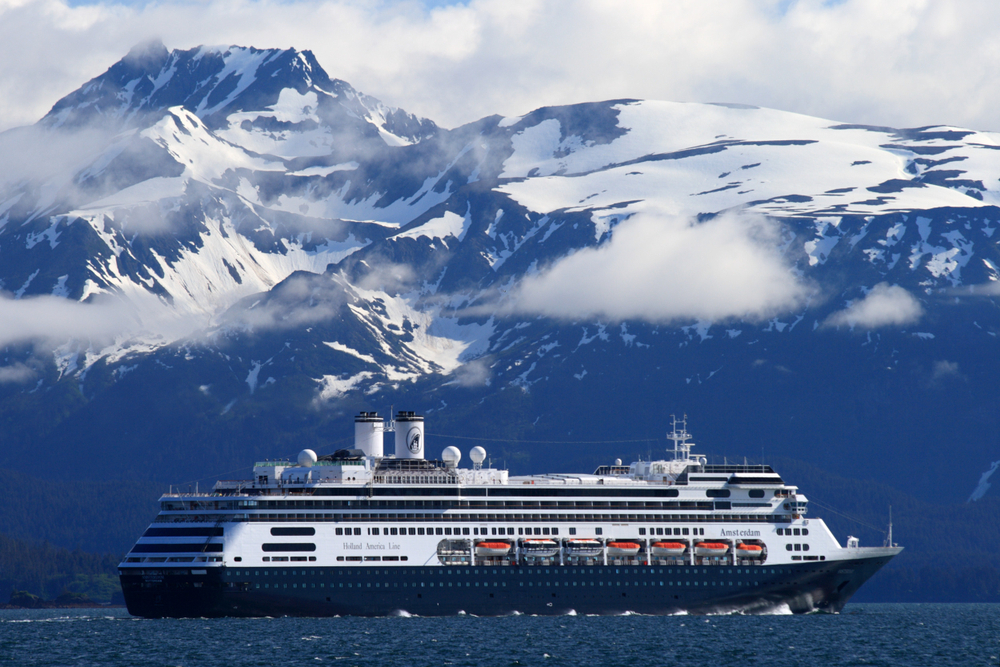 Large blue cruise ship sailing past snowcapped mountains.