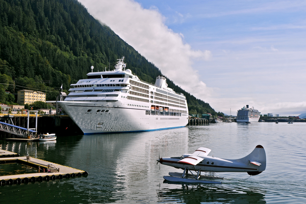 Cruise ship in port with blue water plane landing on water in foreground.