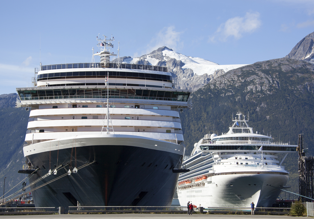 Cruise ships in port with large snowy mountains in background.