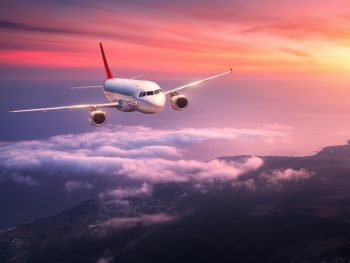 white passenger airline flying during sunset over clouds, with ocean below