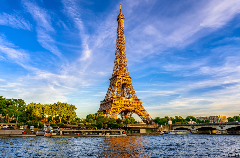 Iron Eiffel Tower with blue sky in background and blue waters in foreground.