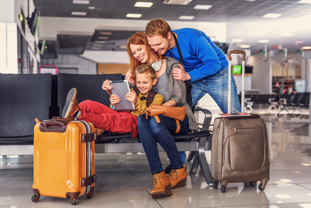 Family of three- caucasian mother, father and son watching screen of personal computer with two carryon suitcases with them.
How to pack lightly using only a carryon.