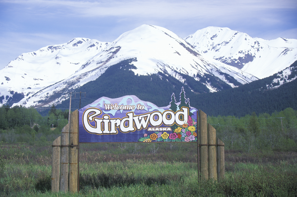 Colorful wooden welcome to Girdwood Alaska with snow-capped mountains in background.