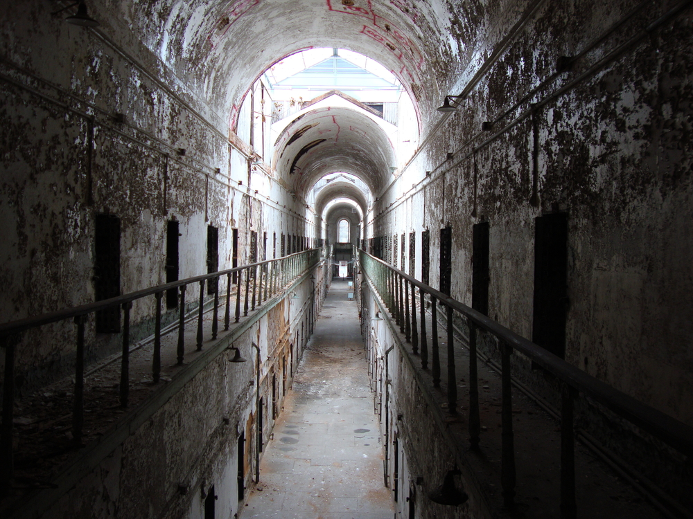 Looking down a long hallway in a dilapidated prison. There is paint peeling off of the walls, part of the hallway are dark, and it is two floors with rows and rows of cell doors. Its one of the best things to do in Philadelphia. 