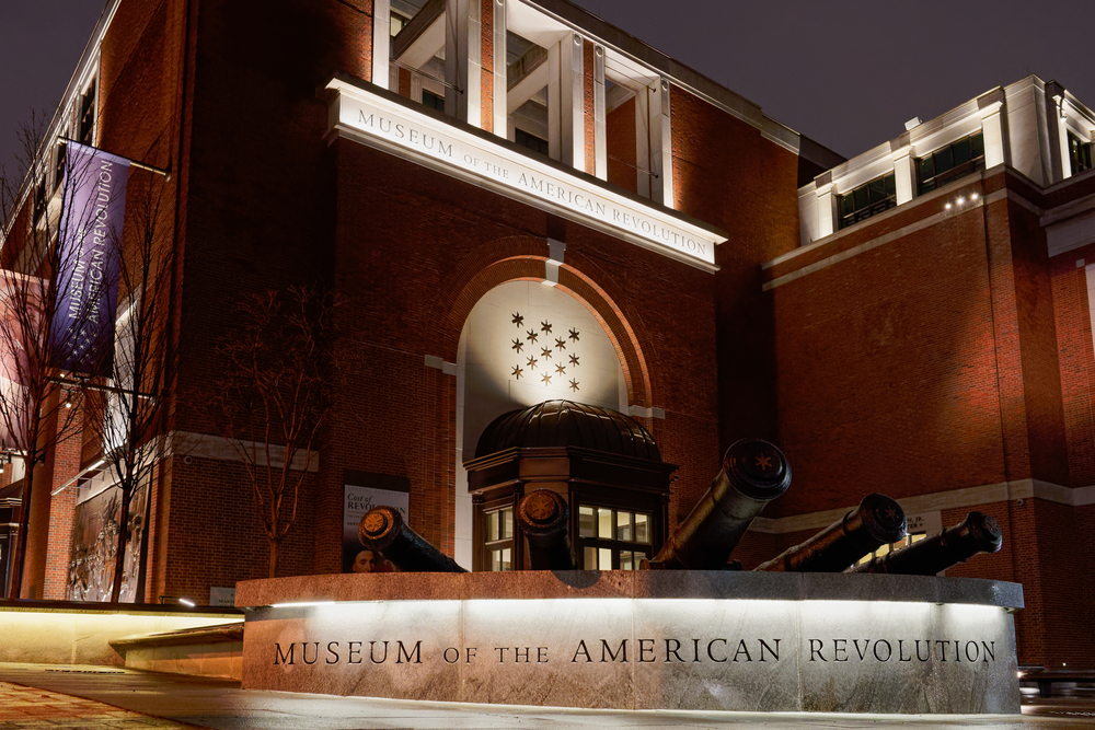 The outside of the Museum of the American Revolution. It is a large brick building. It is night time so parts of the building are lit up.