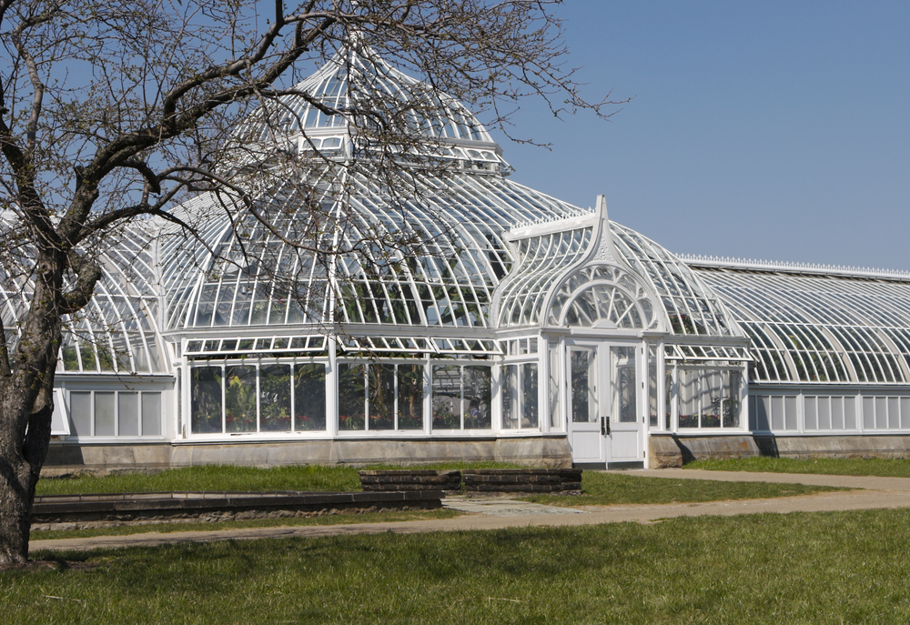 The exterior of the Phipps Conservatory. It is an antique building that looks like it is made of white wrought iron or wood. It has floor to ceiling windows and even the ceiling is windows. It has a large center dome with a set of double doors in front of the dome. Its one of the best things to do in Pittsburgh.