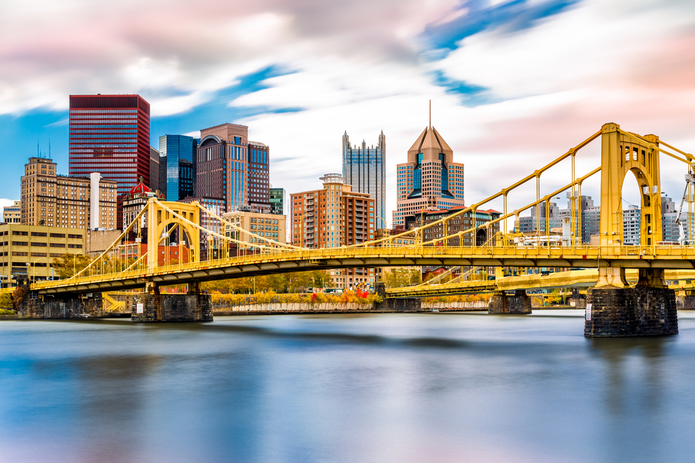 A view of the Pittsburgh skyline from the Allegheny River. You can see two bright yellow bridges crossing the river and skyscrapers. 