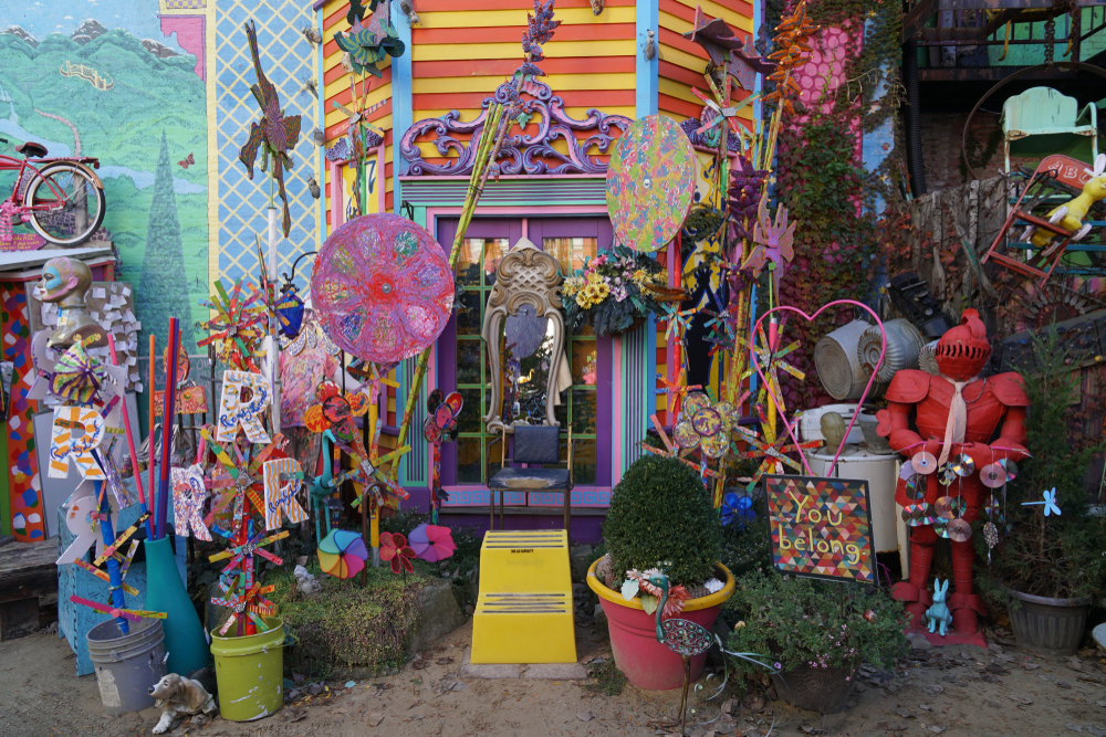 An collection of colorful found objects in front of a wall at Randyland, one of the best things to do in Pittsburgh. There are colorful mirrors, sculptures, chairs, mosaics, and more.