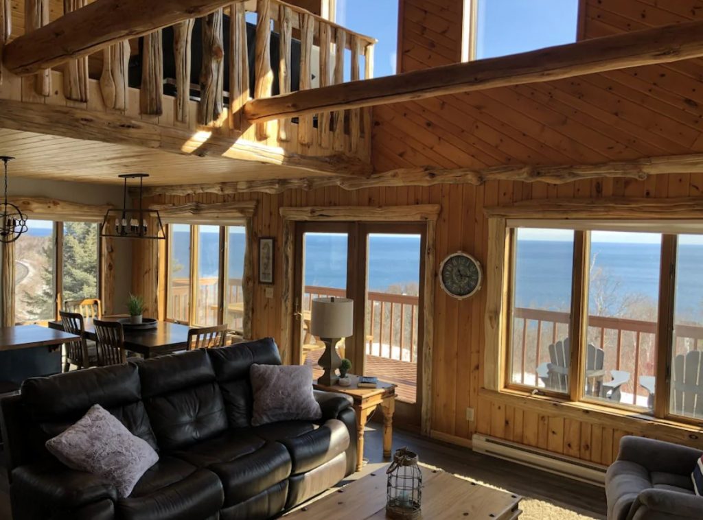 The interior of a classic log cabin that sits on the shore of Lake Superior. You can see the lake from the many windows in the living area. 