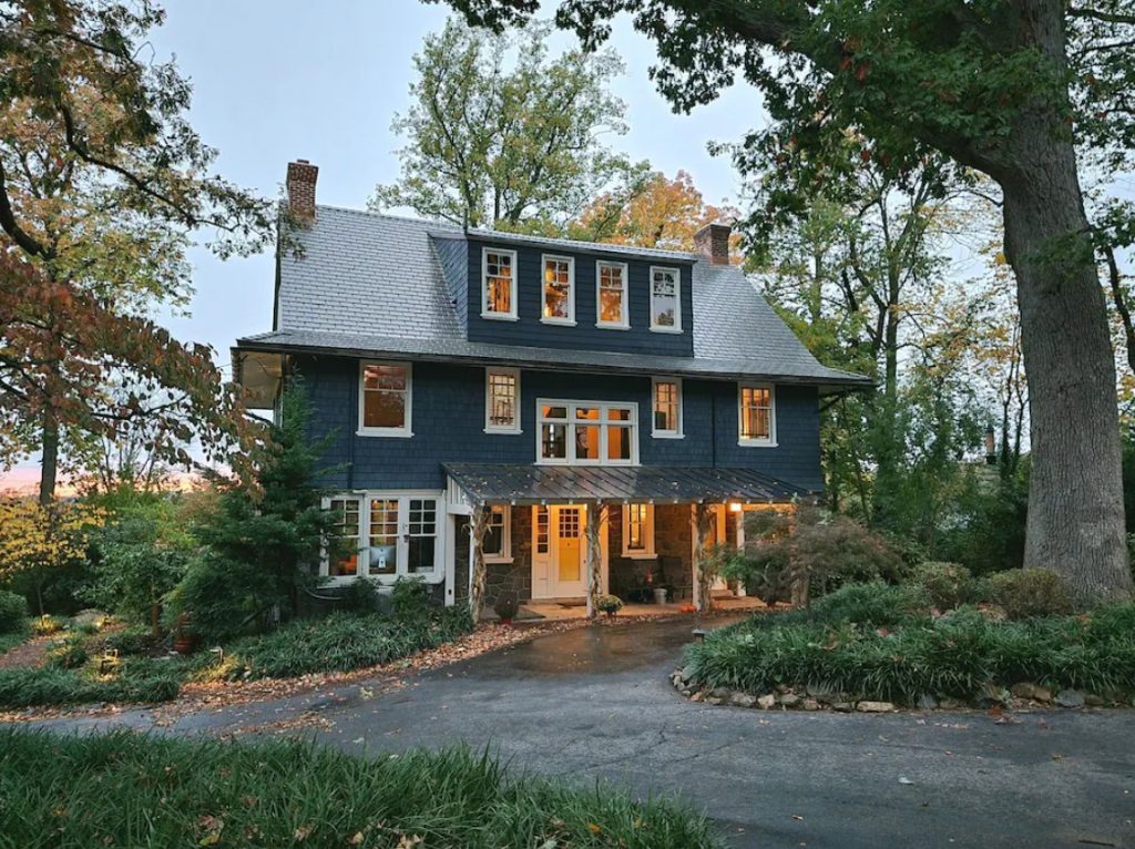 Large craftsman-styled house on wooded lot with leaves changing for autumn. Large circular driveway in front of house.