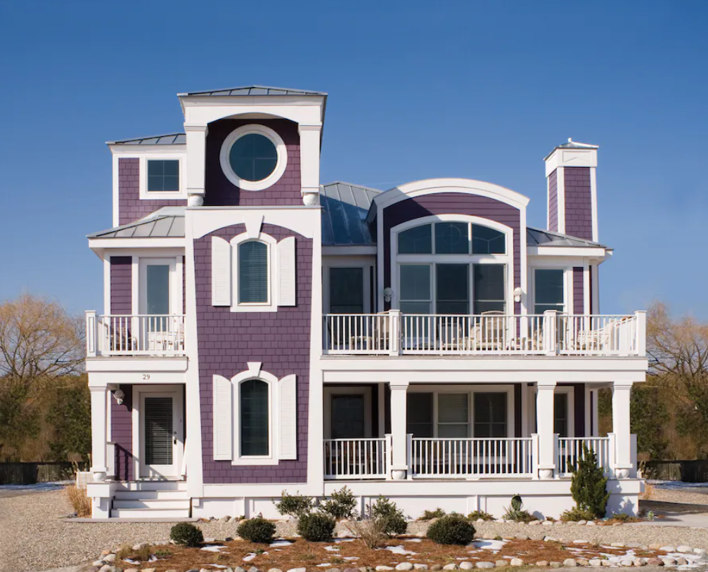 A large purple beach house with several decks, large windows, and a sandy yard. One of the best Delaware Airbnbs. 