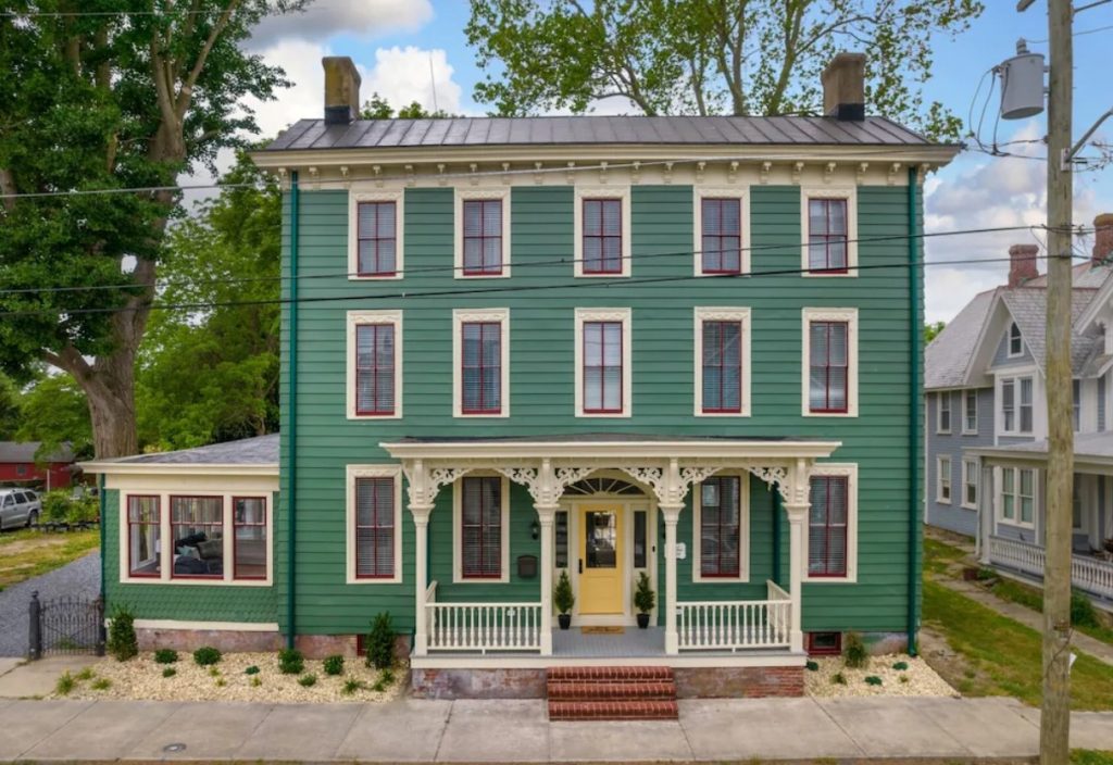 A large green Victorian style home with lots of windows, a front porch, and screened in side porch. It has a pale yellow door. One of the best Delaware Airbnbs. 