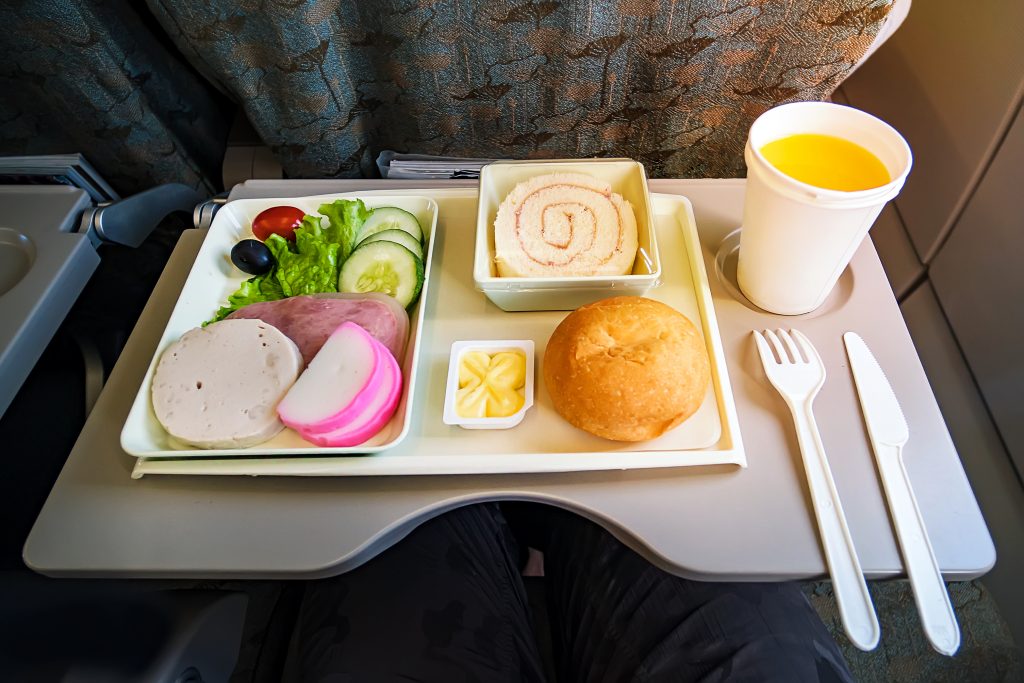 Tray of airplane food with lettuce, cake, roll + butter, glass of orange juice, and fork + knife. 7 tips for surviving long haul flights.