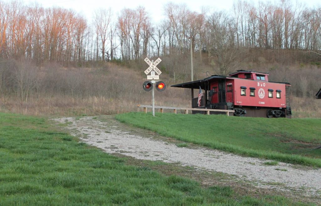 An antique red caboose in a field with a railroad crossing sign next to it. 
