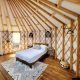 The inside of a large yurt where there is a bed with white sheets, black wicker lights, a patterned rug, and a large glass door. It's one of the best places for glamping in Ohio.