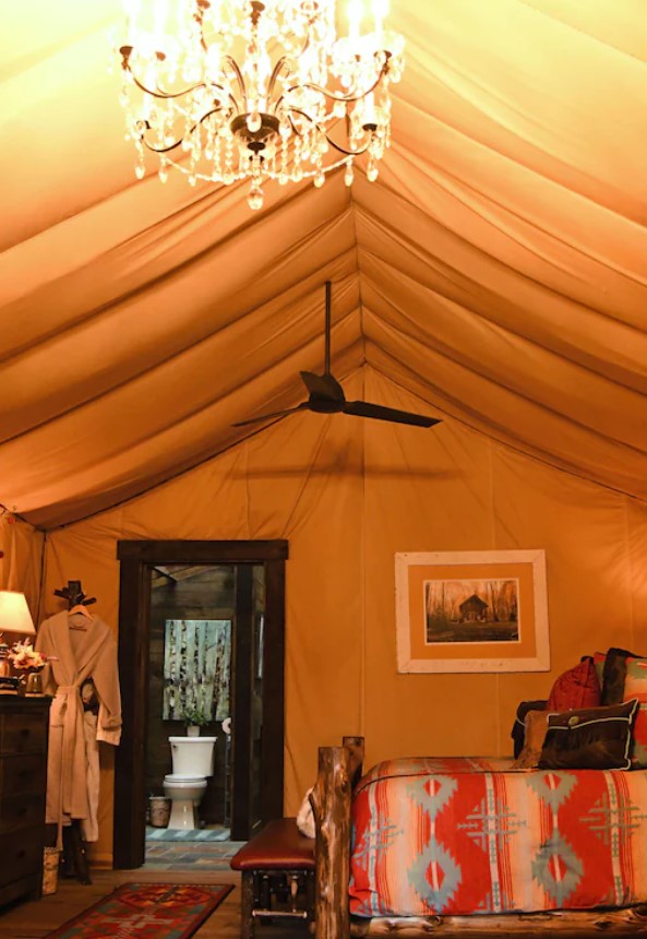 The inside of a luxury tent with a chandelier, a ceiling fan, a king-sized bed, and a private bathroom. It's one of the best places for glamping in Ohio.