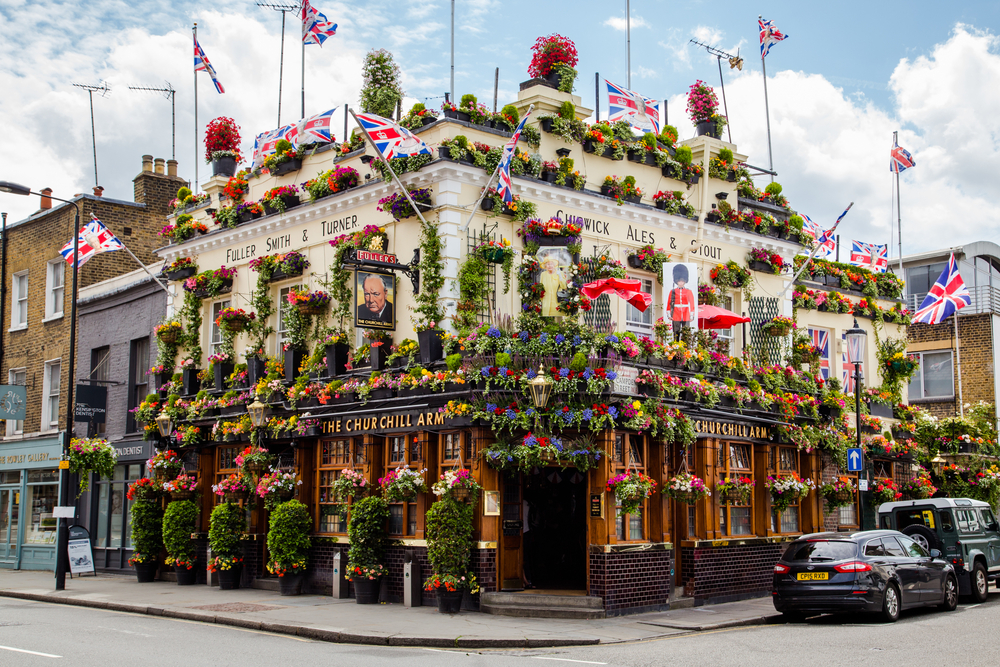 Exterior of the Churchill Arms with many flowers and Union Jack flags.
