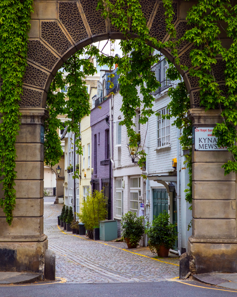 View through a ivy covered arch to the colorful buildings of Kynance Mews.