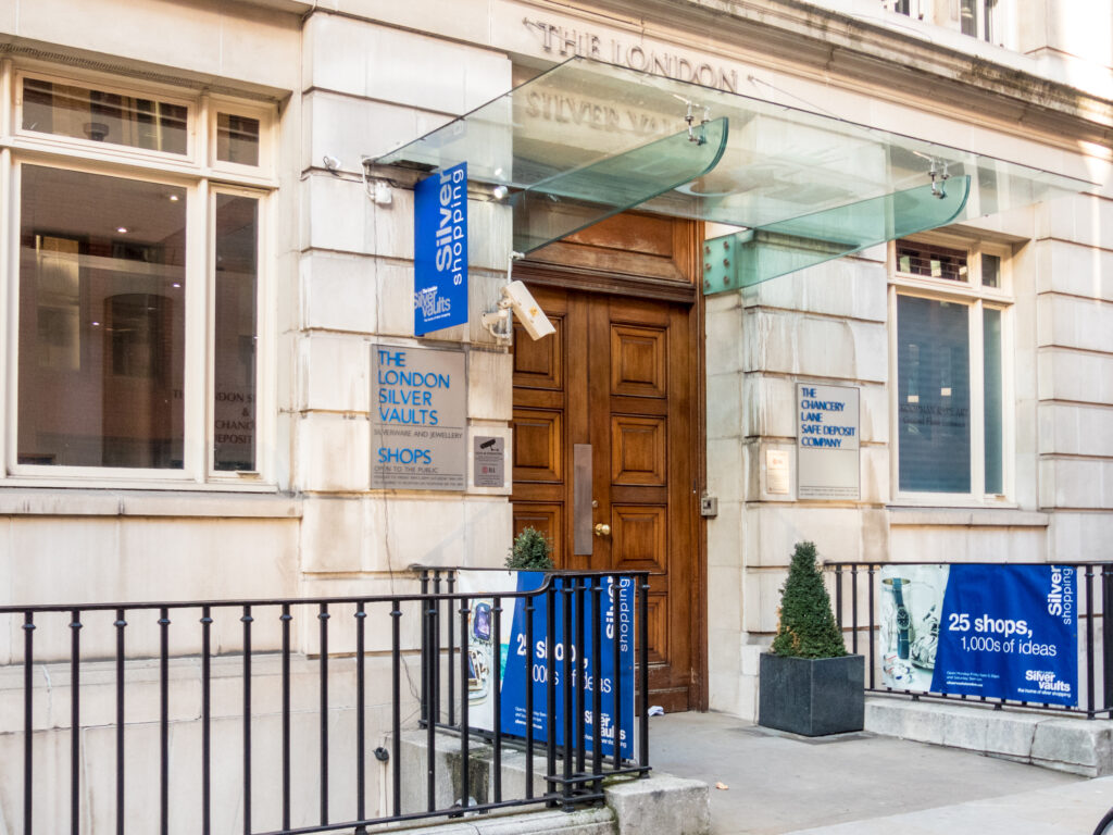 stone building with wooden doors, blue signs in front and wrought iron fencing.