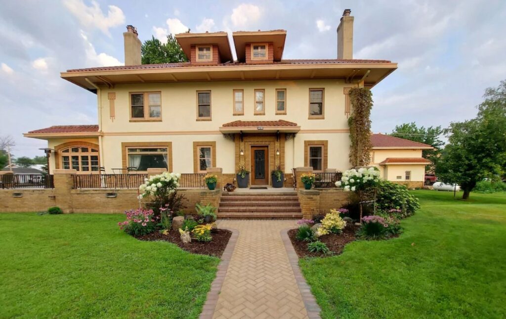 The front exterior of a large historic mansion. It has a brick path leading to a veranda, lots of windows, and two chimneys. One of the best Airbnbs in North Dakota.