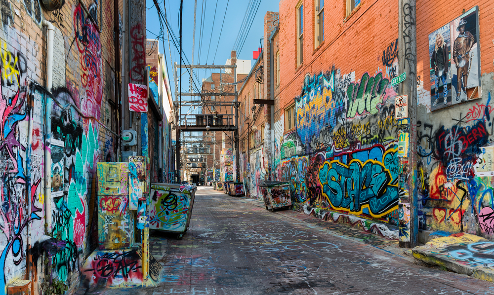 Very colorful street with graffiti painted on red brick walls. Wires overhead.
