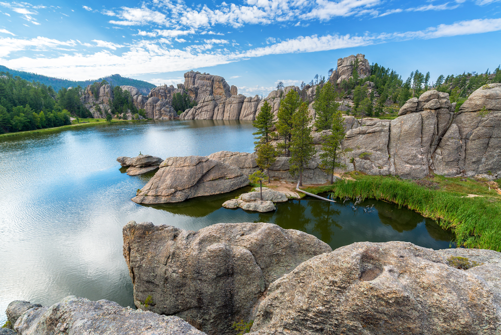 Calm blue lake surrounded by tall rock formations and green evergreen trees. Thing to do near Rapid City SD.