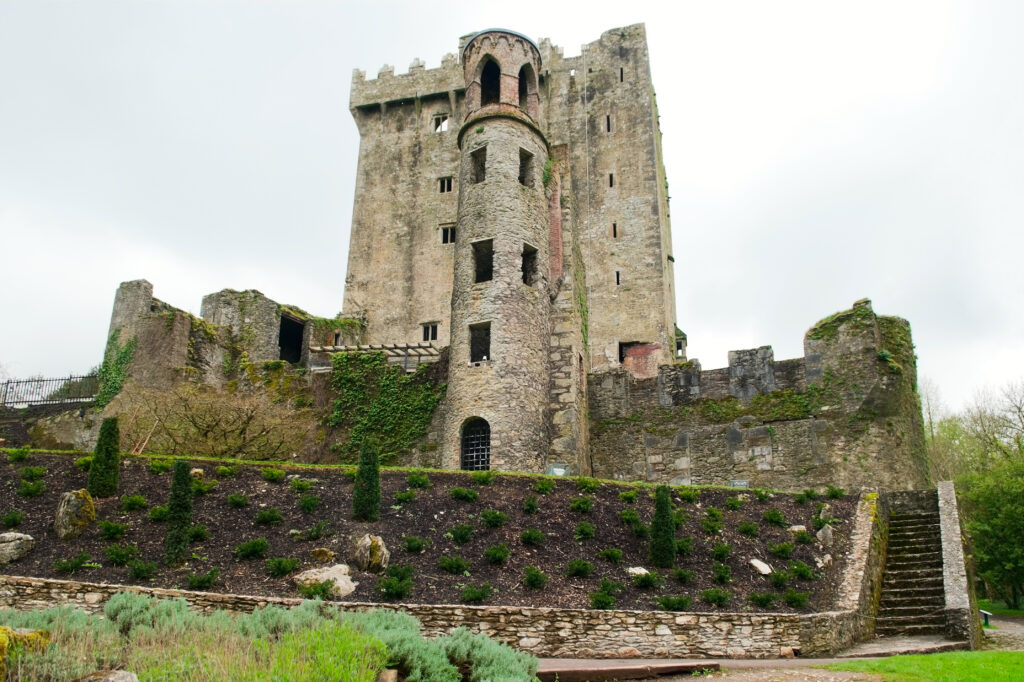 Large stone castle with round turret. Stone fence and stone steps in foreground. Kiss the Blarney Stone
 