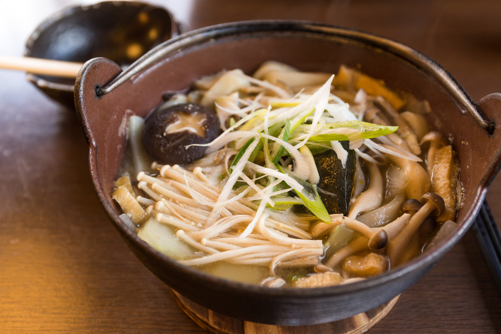 Japanese noodles in broth with mushrooms on top. It is in a brown bowl. 