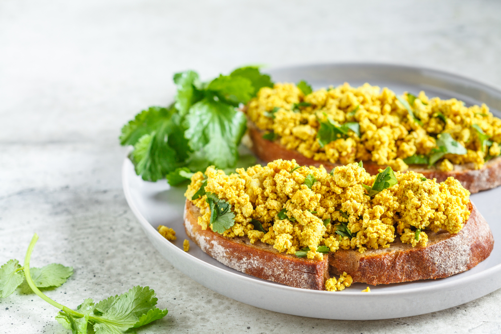 Vegan scrmabled eggs on toast on a plate plate with a green garnish. 