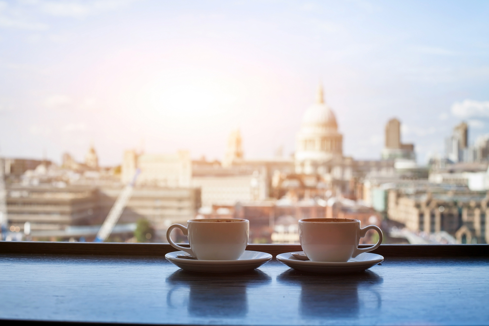 Two coffee cups on a table with a view of London in the background. The article is about the best breakfast in London. 