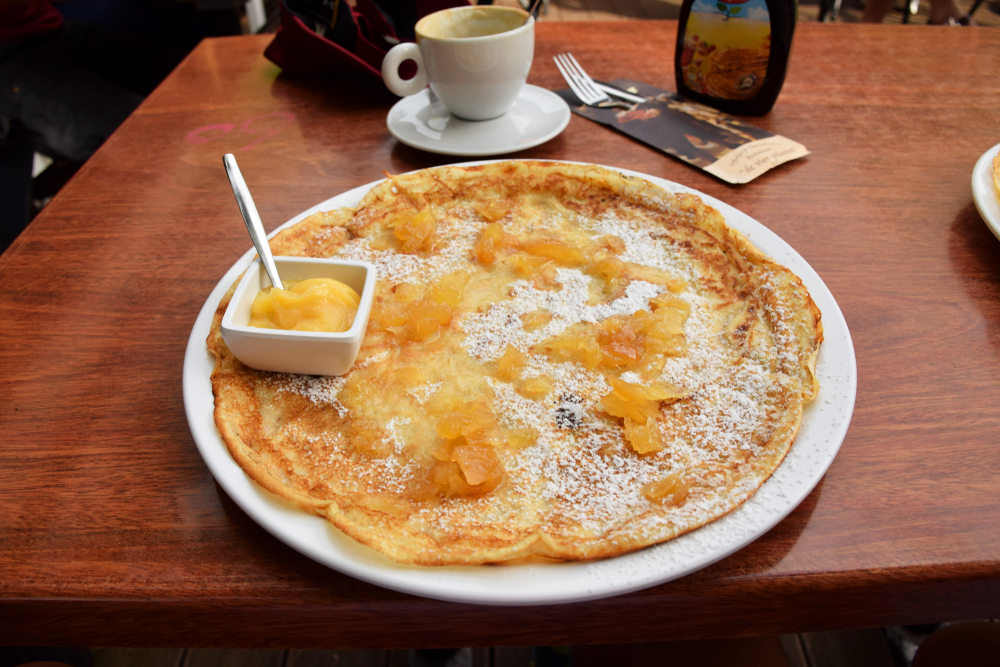 A ginger and custard breakfast pancake on a plate with a cup of coffee beside it.   