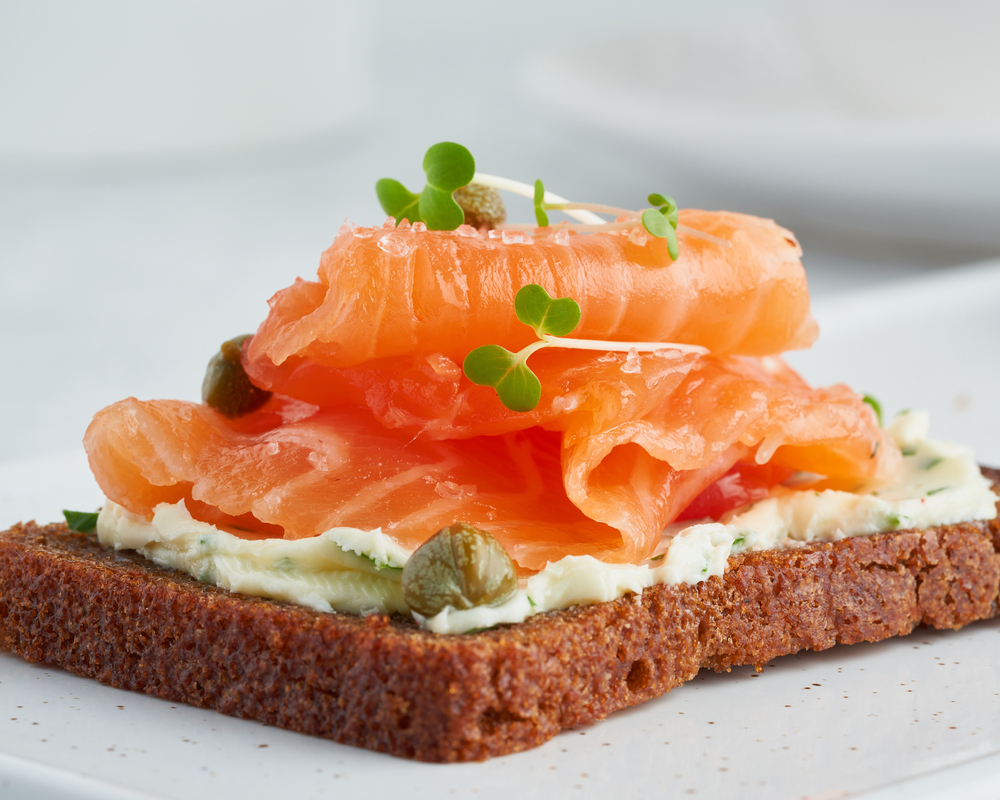 Smorrebrod - traditional scandi sandwiches. Black rye bread with salmon, cream cheese, capers on white background. Side view, close up