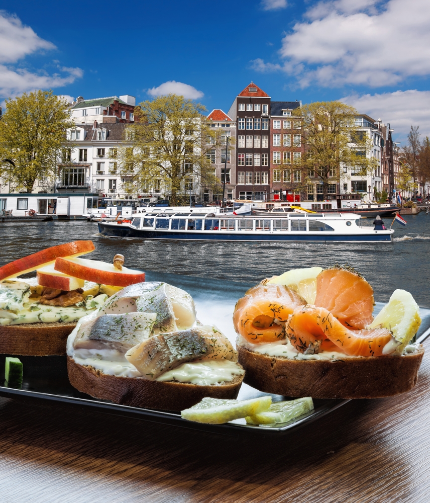 Amsterdam city with breakfast fishplate against tourboat on canal in Netherlands. This article is about breakfast in Amsterdam. 