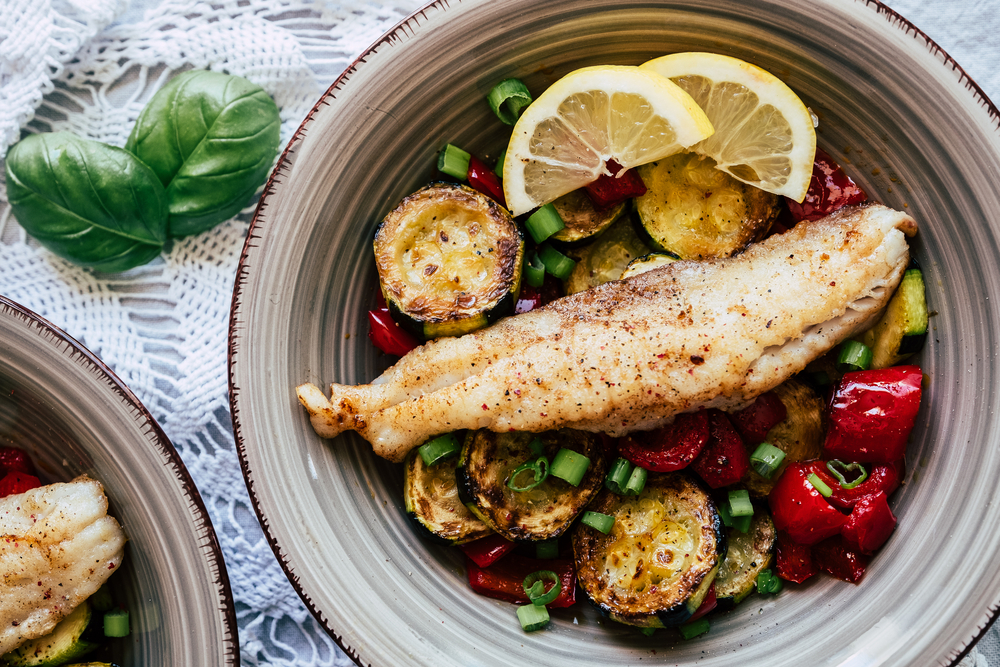 Hake fillet fish dish with zucchini vegetables and fresh lemon peppers