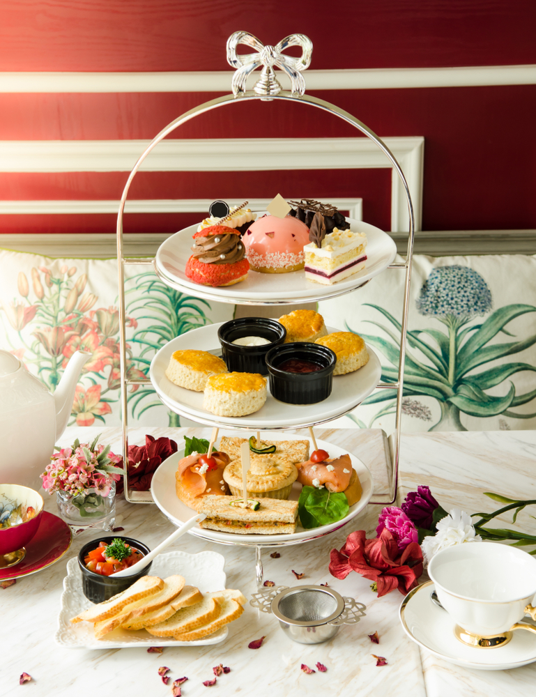 a cake stand with pastries and sandwiches on on a table with two tea cups. 