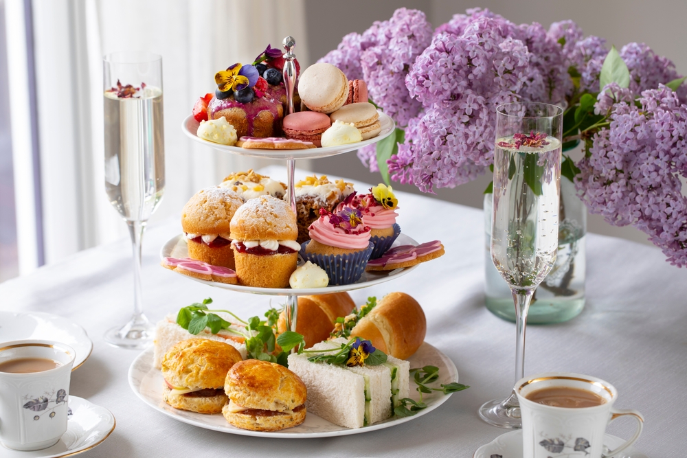 Three-tier tray with delicacies, flute filled with champagne and purple flowers in background at tea in London