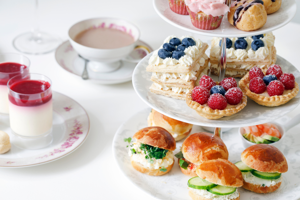 a table with cakes and sandwiches on a  stand and a cup of tea. 