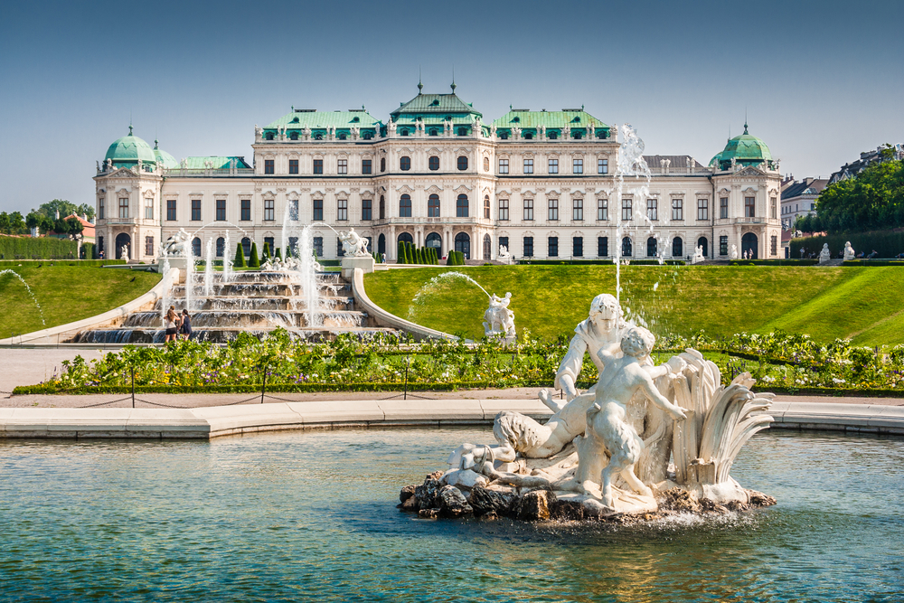 The front of the Belvedere Palace that is now a huge art museum. In front of it is a fountain with an elaborate sculpture. 
