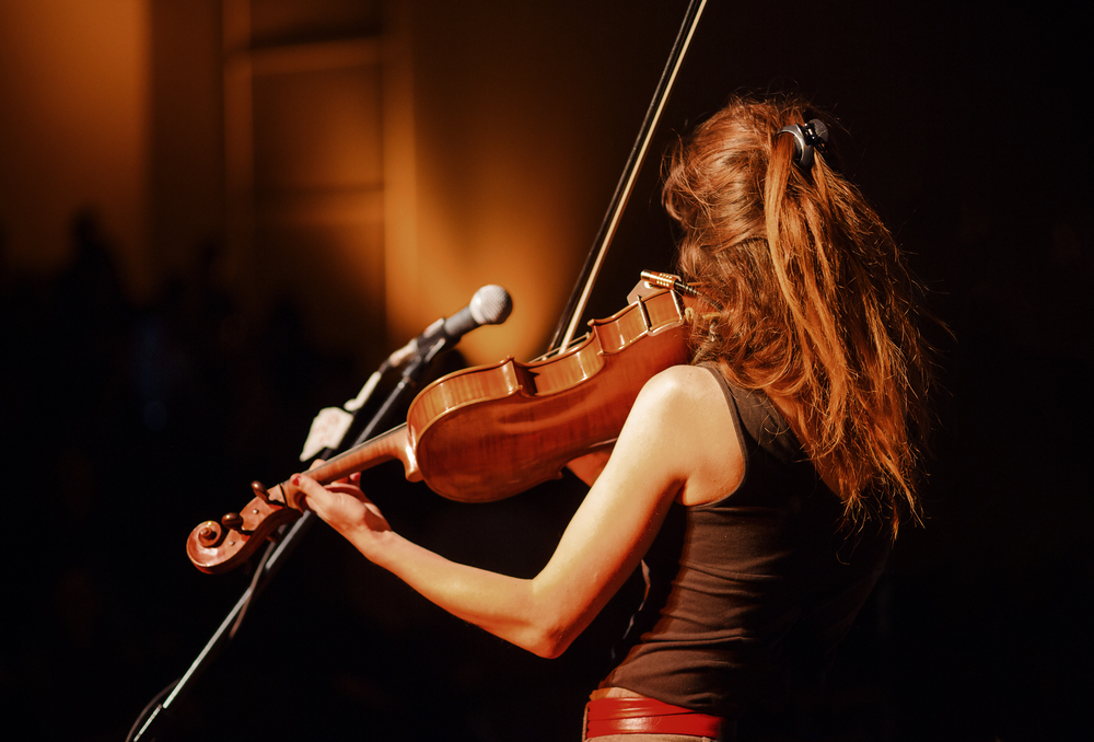 Looking at a woman with red hair from behind as she plays the fiddle on a stage