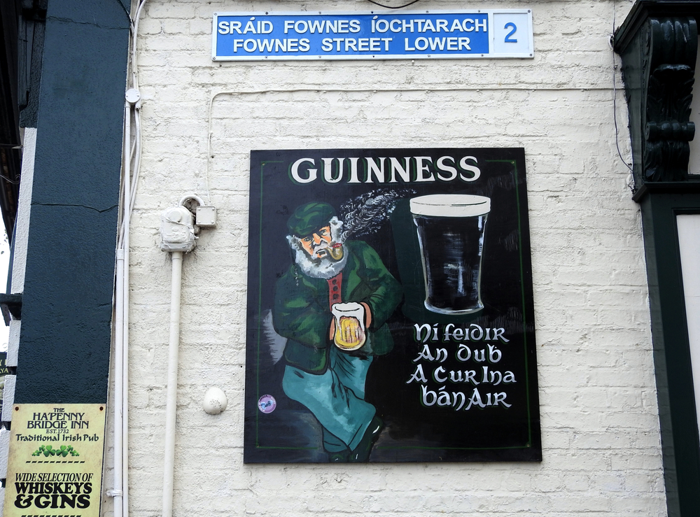 A painted sign advertising Guinness with a man drinking and smoking a pipe. There is a saying Gaelic on the sign