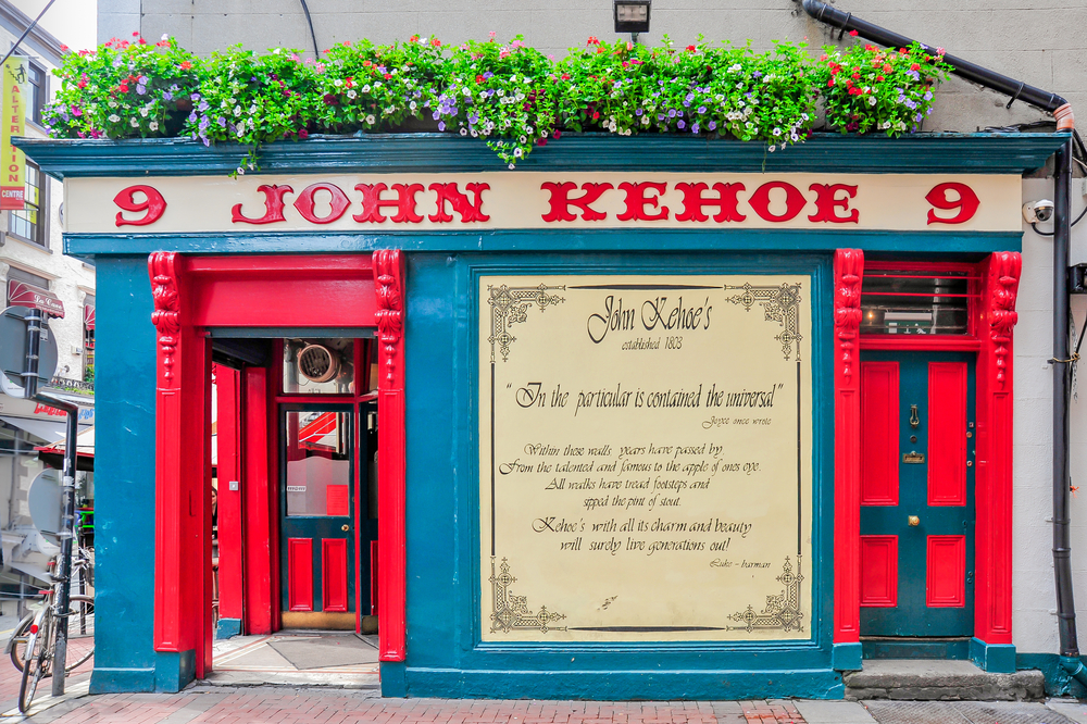 The front of an old pub in Dublin that is painted bright red and blue and has flower boxes along the top of it