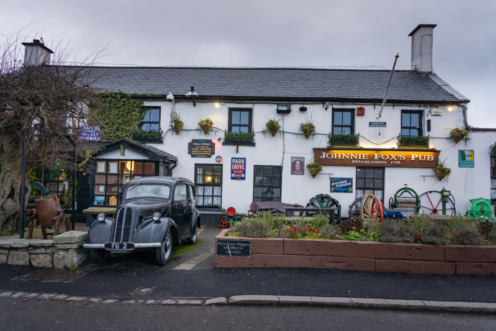 The front exterior of a large white building that is Johnnie Fox's Pub as the sun is setting