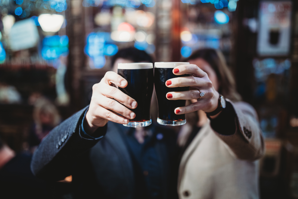 A close up of two people clinking pints of Guinness together in a bar