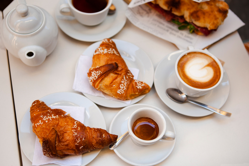 Tablee with croissant and hot black coffee against a white table. 