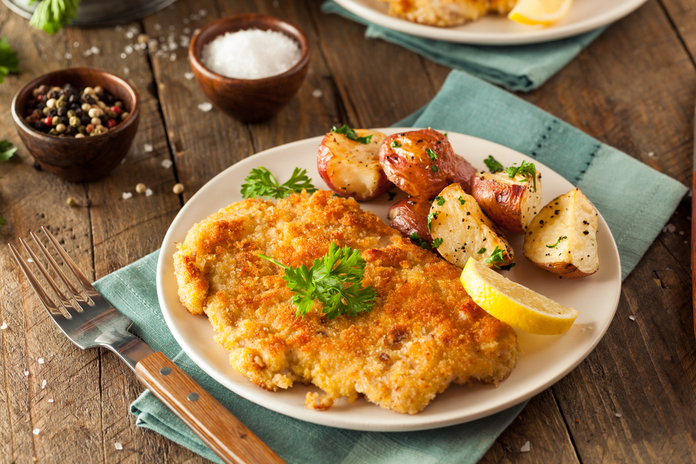 breaded schnitzel in white plate on green cloth restaurants in Vienna