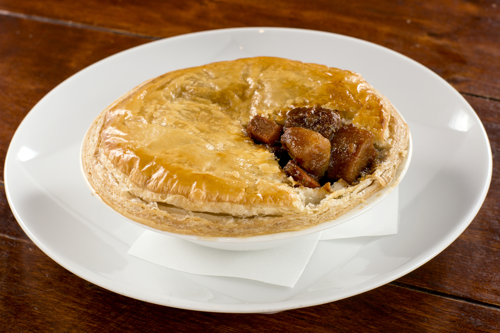 A white plate with a small steak and Guinness pie on it with the top cut open so you can see whats inside the pie