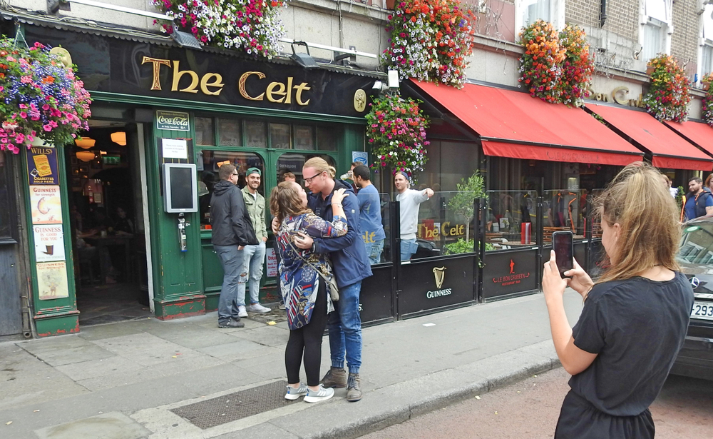 A couple posing outside of The Celt a pub in Dublin, while someone takes their picture. 