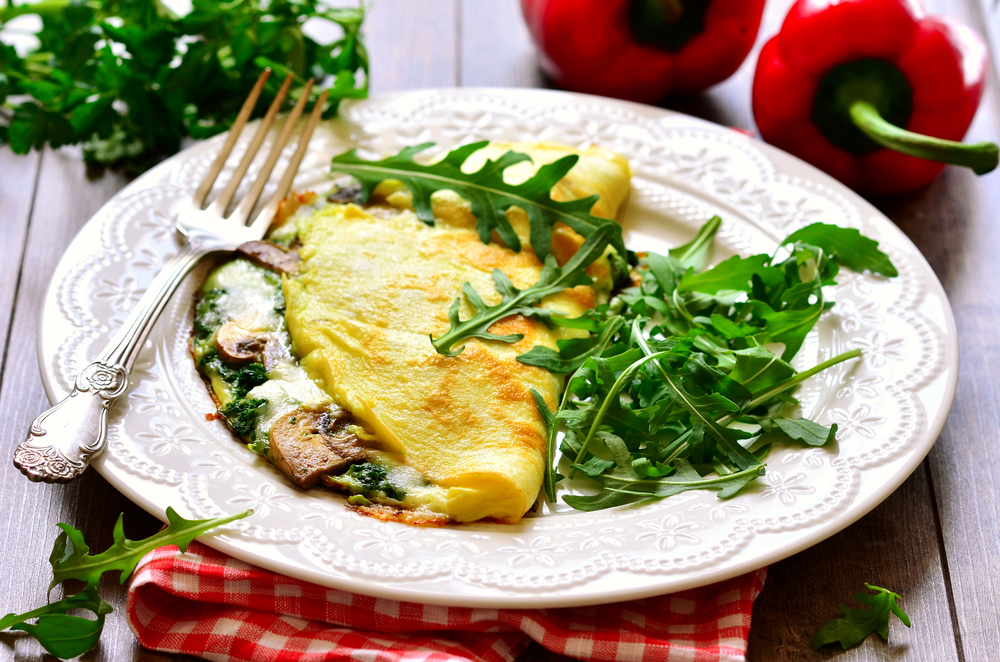 Omelet stuffed with spinach and mushrooms on a white plate.