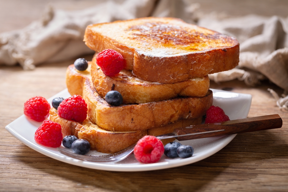 thich slices of bread piled on white plate with maple syrup & berries as garnish during brunch in London